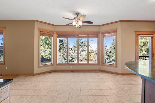 unfurnished dining area with crown molding, baseboards, light tile patterned floors, a textured ceiling, and a ceiling fan