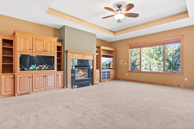 unfurnished living room with ceiling fan, baseboards, carpet, a premium fireplace, and a raised ceiling