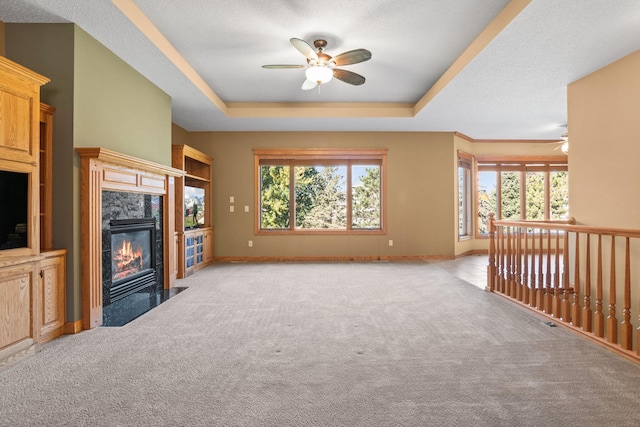 unfurnished living room featuring a tray ceiling, light colored carpet, a fireplace, and a ceiling fan