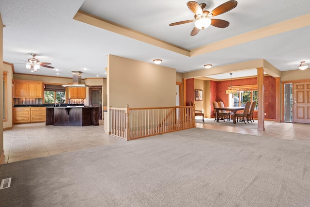 unfurnished living room with visible vents, ceiling fan, light colored carpet, light tile patterned floors, and a raised ceiling