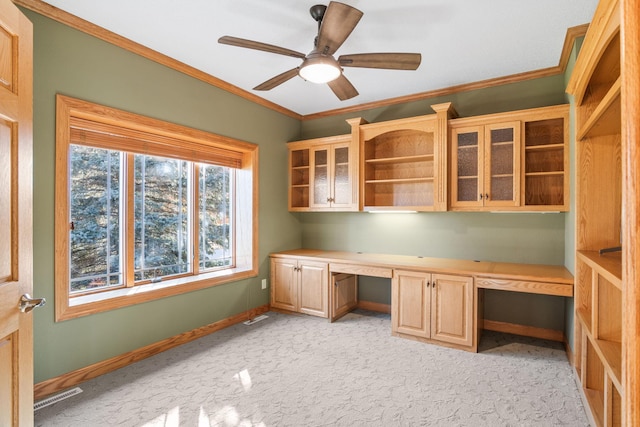 unfurnished office featuring visible vents, a ceiling fan, built in desk, crown molding, and baseboards