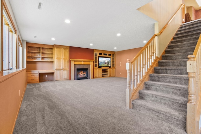 unfurnished living room featuring visible vents, built in desk, recessed lighting, carpet floors, and a tile fireplace