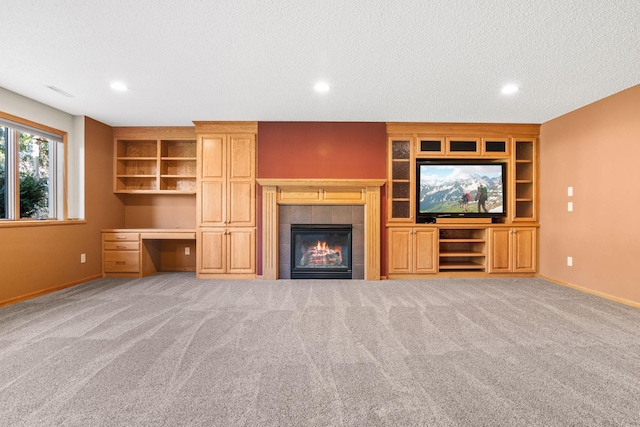 unfurnished living room with carpet, baseboards, built in study area, a fireplace, and a textured ceiling