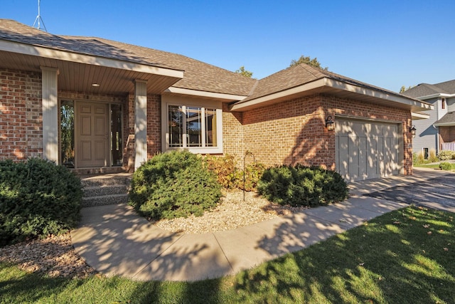 view of front of home featuring an attached garage, brick siding, driveway, and roof with shingles