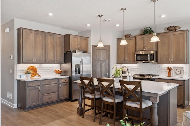 kitchen with a center island with sink, light wood-style flooring, stainless steel appliances, light countertops, and a kitchen bar