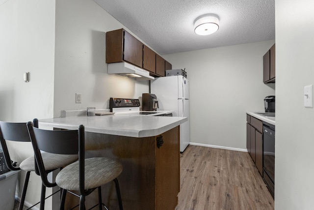 kitchen with a kitchen bar, under cabinet range hood, freestanding refrigerator, a peninsula, and stove