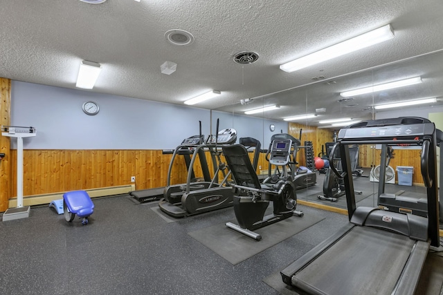 exercise room featuring wooden walls, visible vents, wainscoting, and a textured ceiling