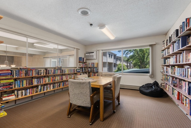 carpeted office with a wall mounted air conditioner, a textured ceiling, and bookshelves