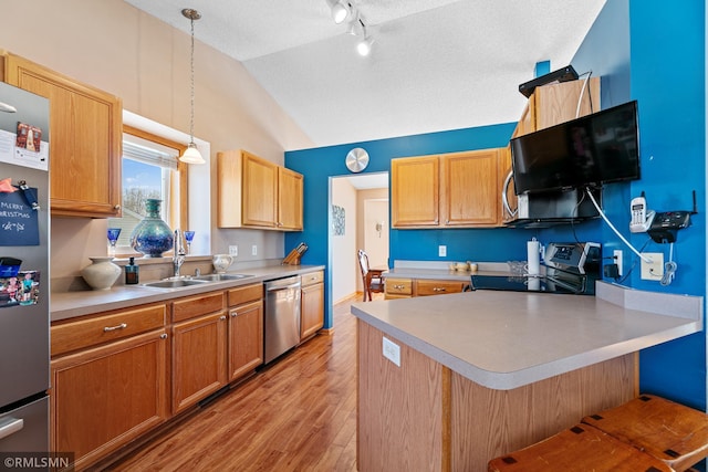 kitchen featuring light wood finished floors, lofted ceiling, a sink, light countertops, and appliances with stainless steel finishes