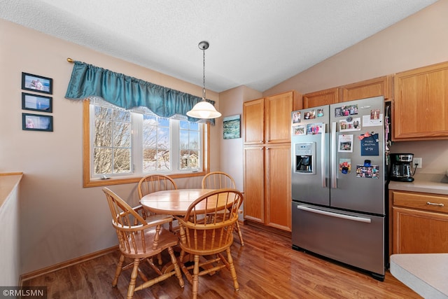 dining space with lofted ceiling, light wood-style floors, baseboards, and a textured ceiling