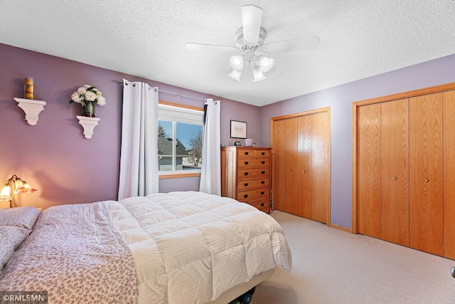 bedroom featuring multiple closets, a textured ceiling, carpet floors, and ceiling fan