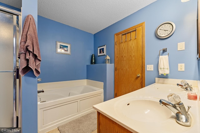 bathroom with double vanity, a textured ceiling, a garden tub, and a sink