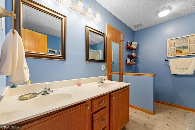 bathroom featuring a textured ceiling, double vanity, visible vents, and a sink