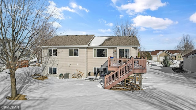 snow covered rear of property featuring central air condition unit, roof with shingles, a deck, and stairs