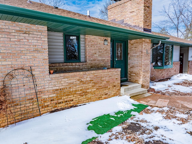 snow covered property entrance with brick siding and a chimney