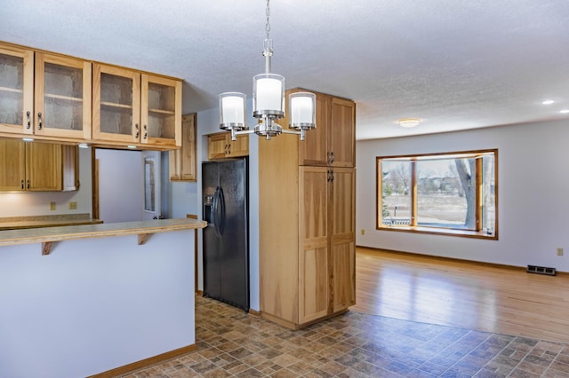 kitchen featuring hanging light fixtures, a kitchen breakfast bar, glass insert cabinets, and black refrigerator with ice dispenser