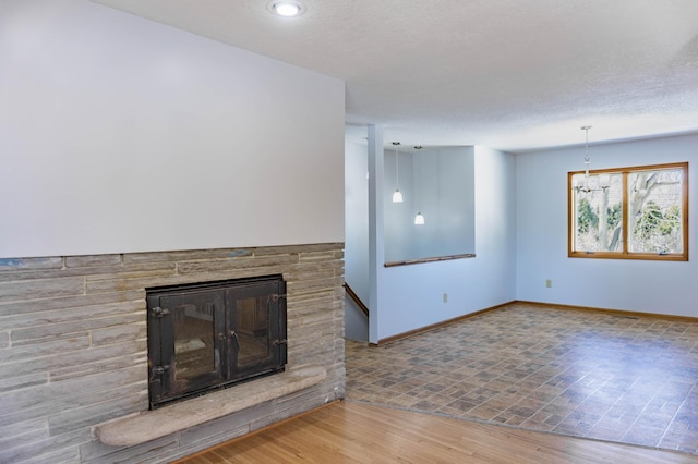 unfurnished living room featuring a stone fireplace, wood finished floors, baseboards, and a textured ceiling