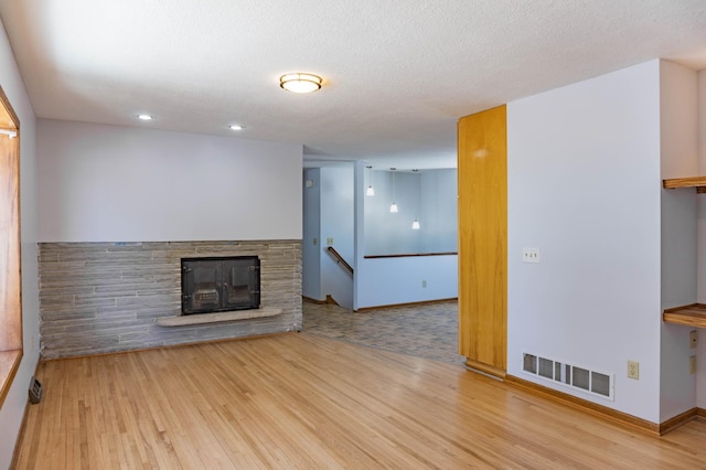 unfurnished living room featuring a stone fireplace, wood finished floors, and visible vents