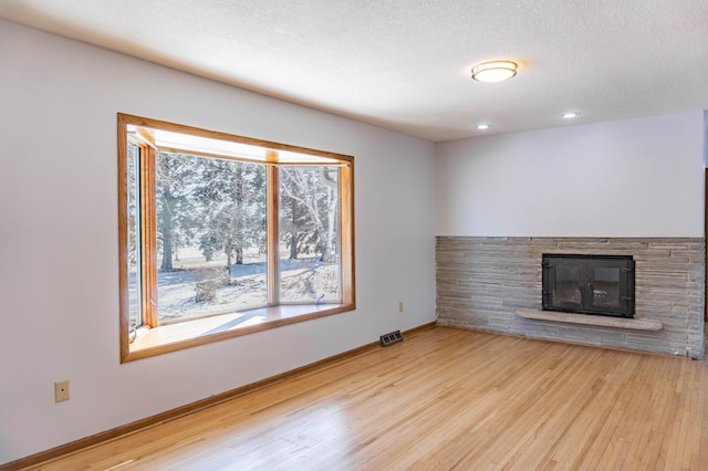 unfurnished living room featuring visible vents, baseboards, a fireplace, light wood-style floors, and a textured ceiling