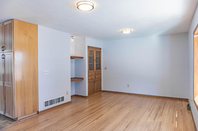 unfurnished room featuring visible vents, baseboards, built in desk, and light wood finished floors