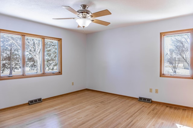 empty room featuring light wood finished floors, visible vents, a ceiling fan, and baseboards