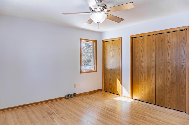 unfurnished bedroom featuring a ceiling fan, visible vents, baseboards, multiple closets, and light wood-type flooring