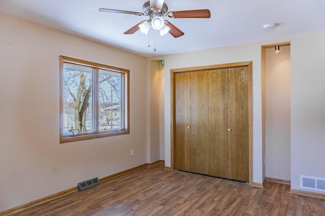 unfurnished bedroom featuring a closet, visible vents, baseboards, and wood finished floors