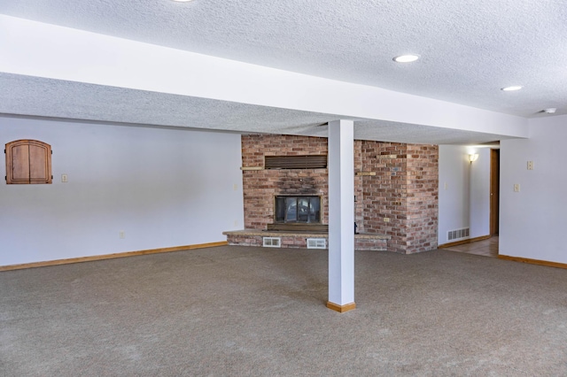 finished below grade area with visible vents, a textured ceiling, carpet floors, baseboards, and a brick fireplace