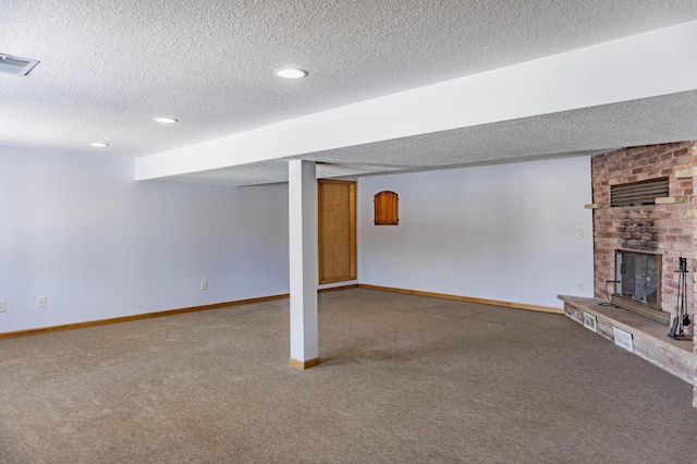 finished below grade area featuring visible vents, a textured ceiling, carpet flooring, baseboards, and a brick fireplace