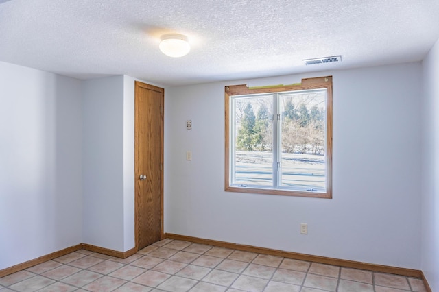 unfurnished room with light tile patterned floors, visible vents, a textured ceiling, and baseboards