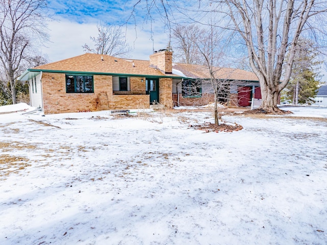 snow covered property featuring a shingled roof, brick siding, and a chimney