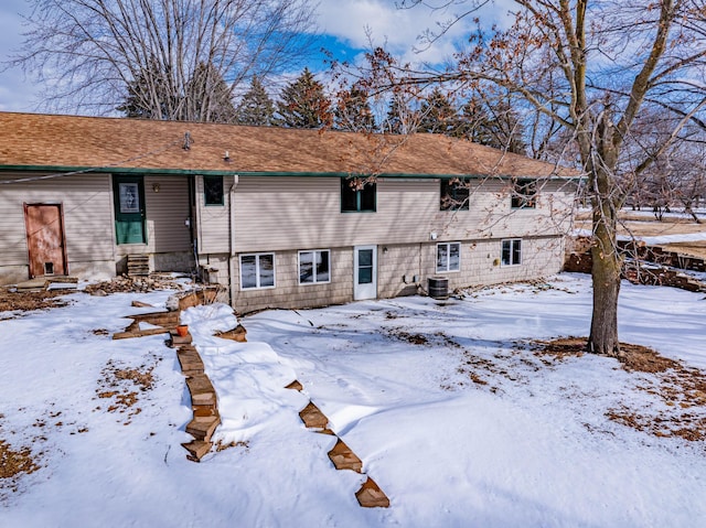 snow covered house with central air condition unit, entry steps, and a garage