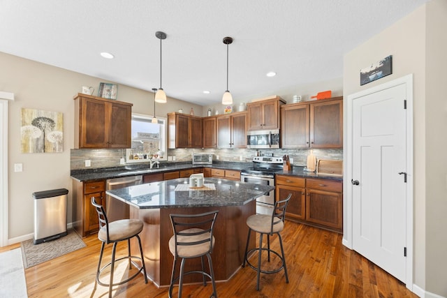 kitchen with decorative backsplash, appliances with stainless steel finishes, a kitchen breakfast bar, and light wood-style floors