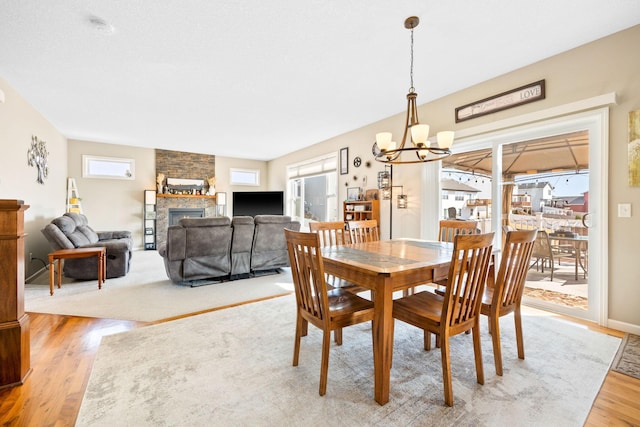 dining space with light wood finished floors, a notable chandelier, a fireplace, and baseboards