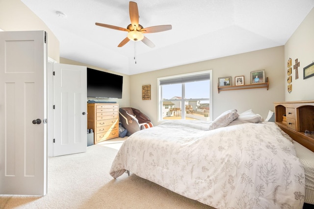 carpeted bedroom with a raised ceiling and ceiling fan