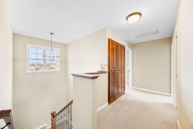 hallway featuring baseboards, an upstairs landing, carpet, and a textured ceiling