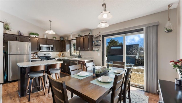 dining space with a wealth of natural light, lofted ceiling, and light wood-style flooring