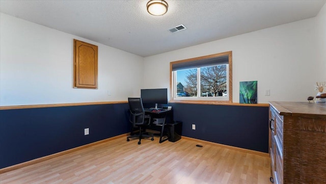 office space featuring visible vents, light wood-style flooring, a textured ceiling, and baseboards