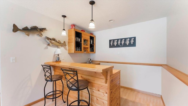 bar with light wood finished floors, a textured ceiling, wet bar, and baseboards