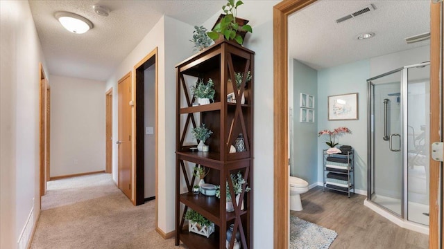 corridor featuring visible vents, baseboards, a textured ceiling, and light wood-style flooring