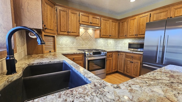 kitchen featuring light stone counters, brown cabinets, stainless steel appliances, and a sink