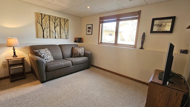 carpeted living area with a drop ceiling and baseboards