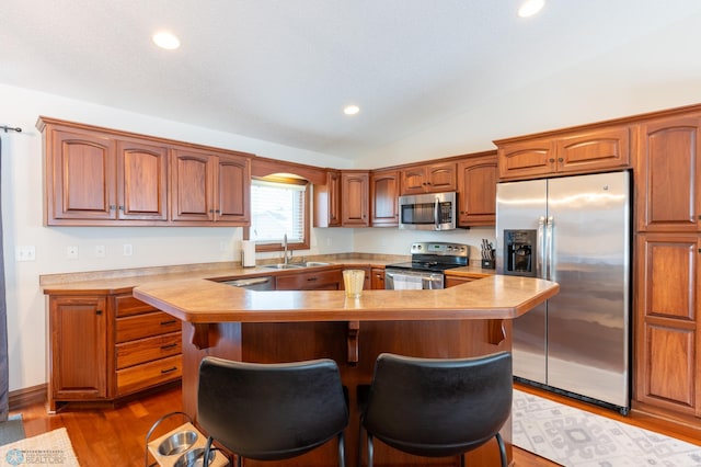 kitchen featuring dark wood finished floors, lofted ceiling, a kitchen breakfast bar, appliances with stainless steel finishes, and a sink