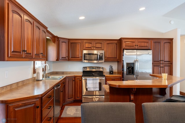 kitchen featuring a breakfast bar, vaulted ceiling, recessed lighting, stainless steel appliances, and a sink