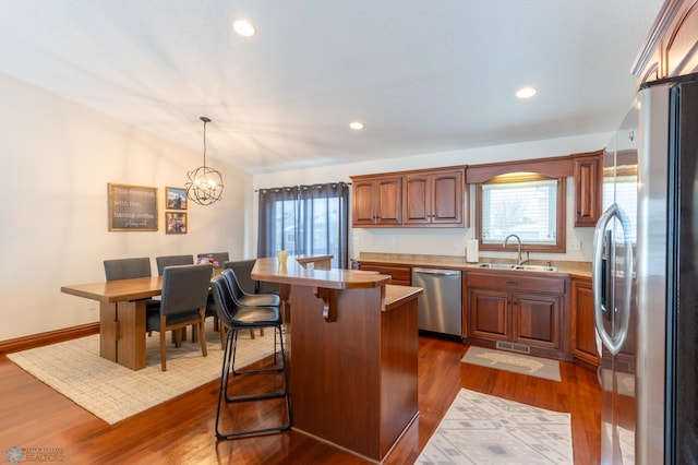 kitchen featuring dark wood-type flooring, a breakfast bar area, vaulted ceiling, stainless steel appliances, and a sink