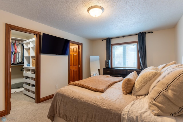 bedroom with a walk in closet, light colored carpet, a closet, and a textured ceiling