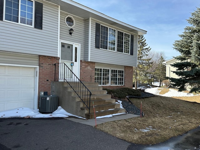 entrance to property with brick siding, an attached garage, and central AC