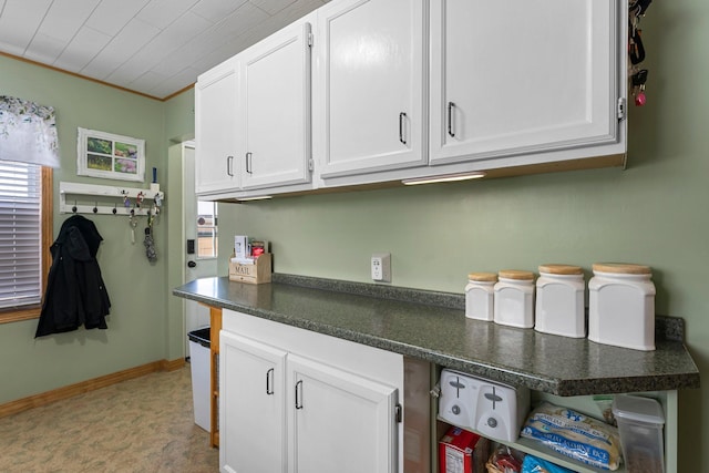 kitchen featuring dark countertops, white cabinetry, baseboards, and ornamental molding