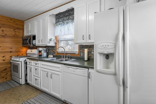 kitchen with white appliances, wooden walls, dark countertops, and a sink