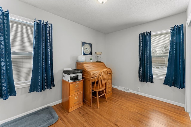 office area with light wood-type flooring, visible vents, baseboards, and a textured ceiling